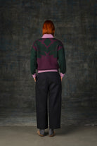 Female model wearing a grape purple bomber jacket with dark green sleeves and pink cuffs. There is an organic pattern inspired by a butterfly's wings on the back of the jacket.